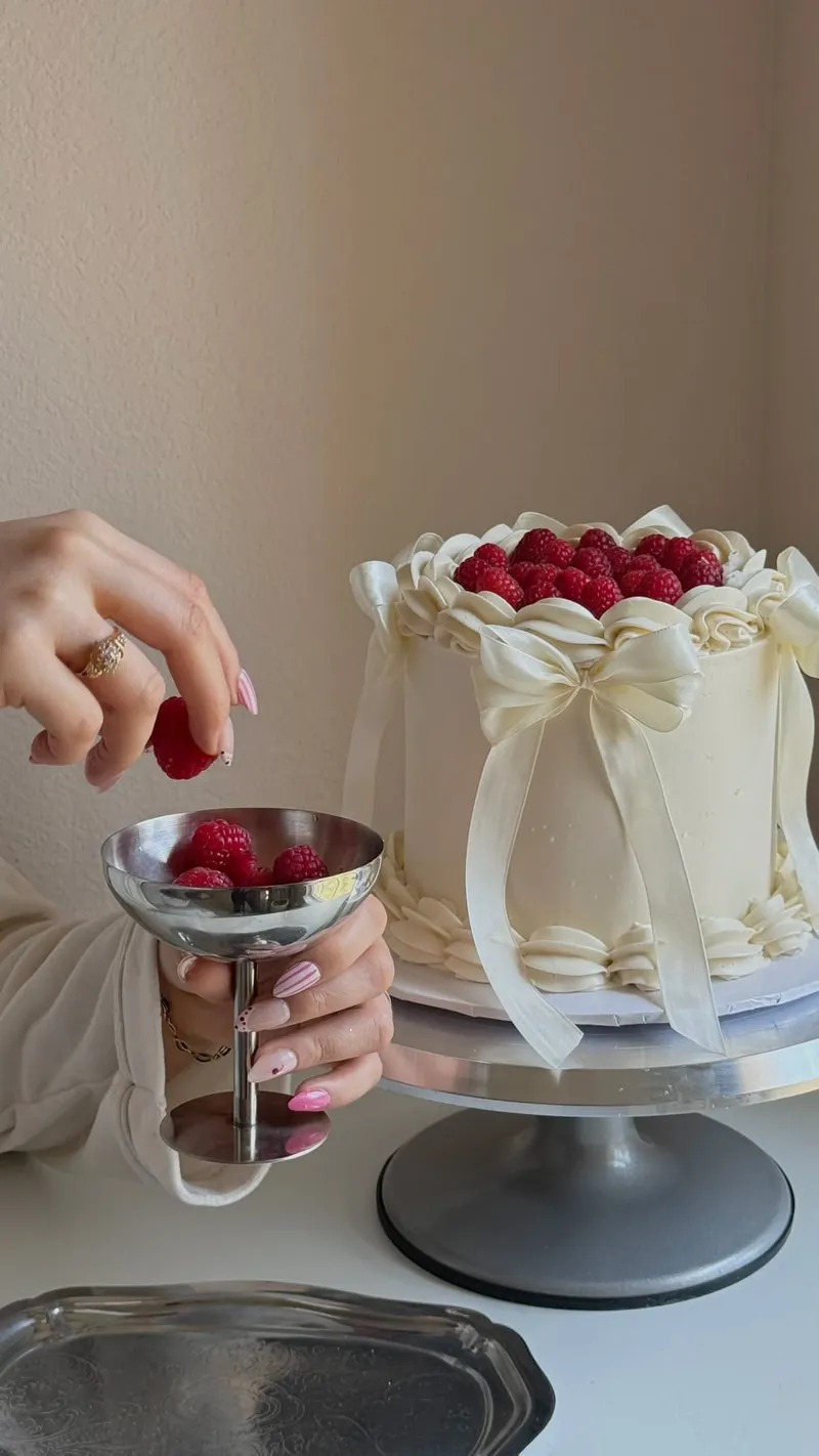 A white birthday cake with raspberries and a fresh manicure