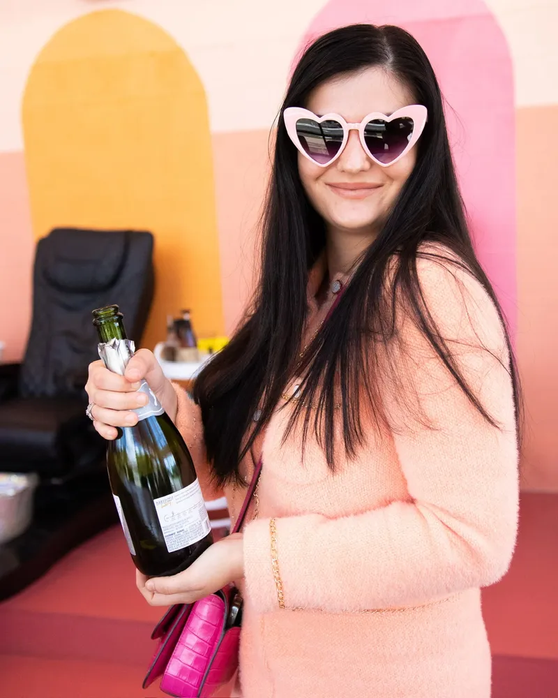 A guest in heart sunglasses with a bottle of bubbly at the salon